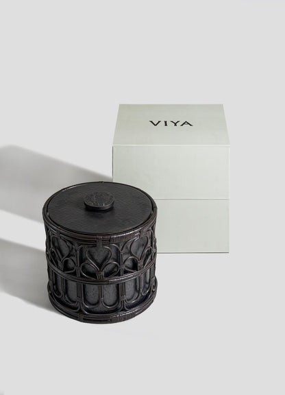 A dark, ornately carved cylindrical Manipur Ice Bucket Large by VIYA sits beside a plain, light-colored VIYA box and elegant barware accessories, all set against a neutral background.