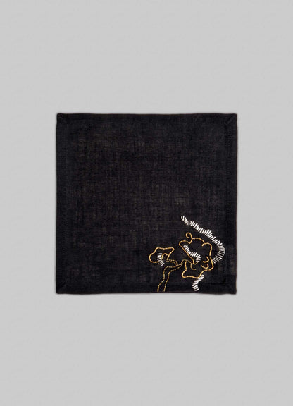 The Viya Blackbuck Dreams Hand Embroidered Black & Gold Cocktail Napkins (Set of 4) feature a dark square design with gold and white abstract embroidery in one corner, shown on a light gray background.