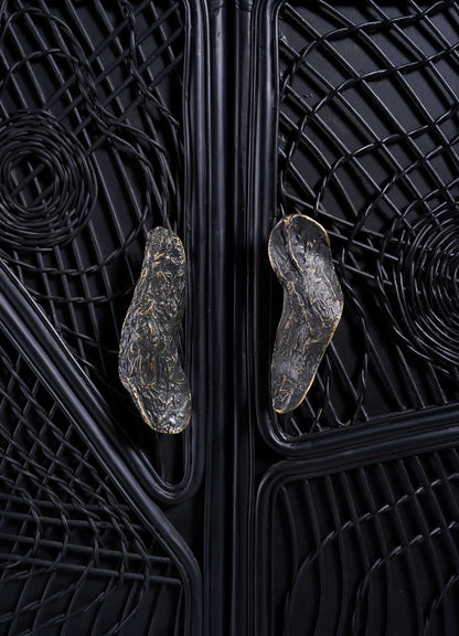 VIYA's Chakra Cabinet features an intricate black textured door with abstract swirling patterns, central organic metallic handles, and subtle cane weaving accents for artisanal detail.