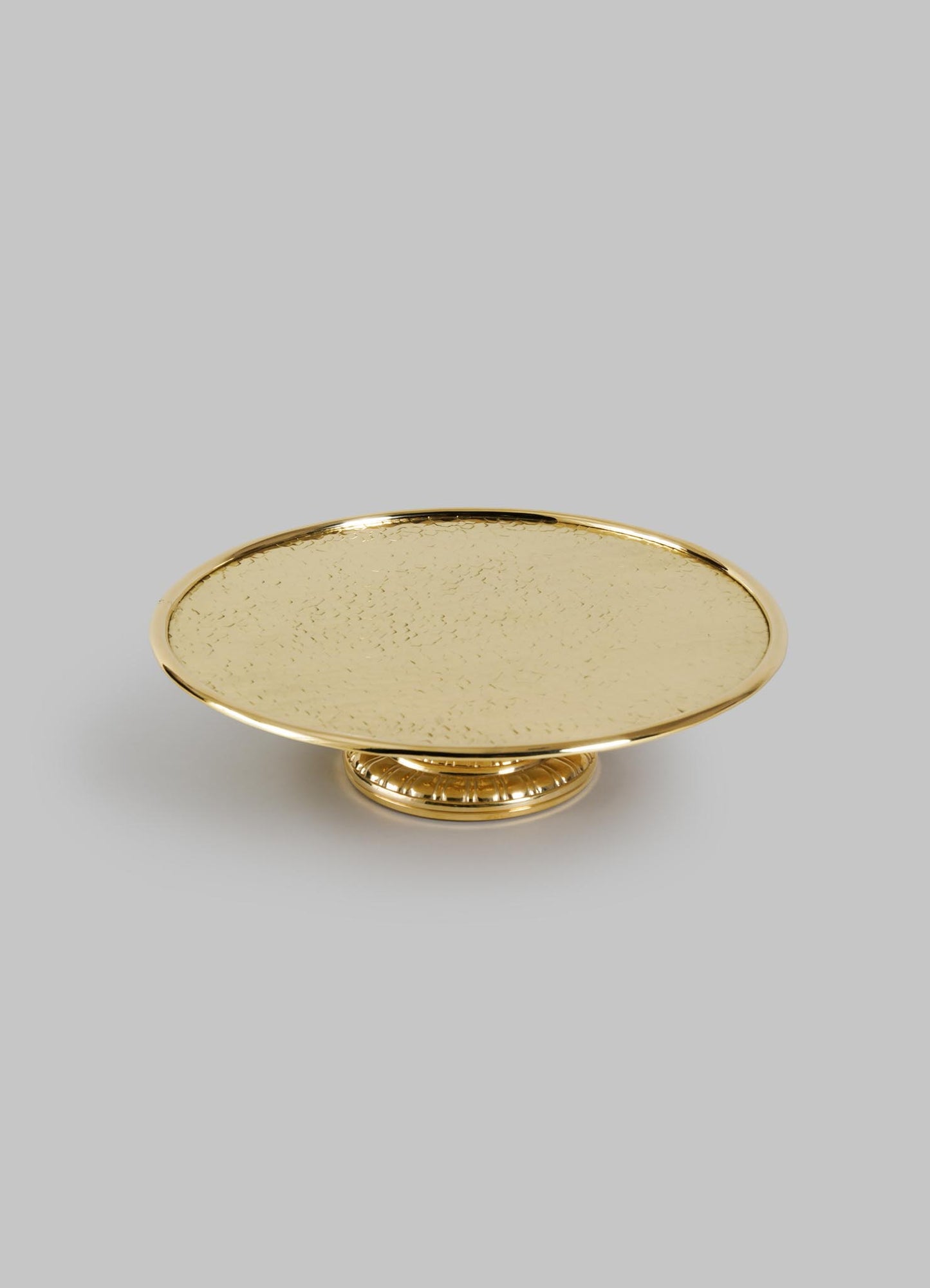 The VIYA City Palace Cake Platter is a round, gold-colored handcrafted brass stand with a textured surface and short decorative pedestal base, shown against a plain light gray background.