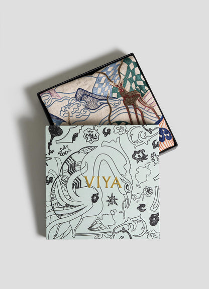 A decorative box with "Viya" in gold on a pale background opens to reveal the Dreamscape Red Embroidered Cushion Cover A (24"x24"), featuring vibrant abstract patterns and motifs inspired by Rajput manuscript art.