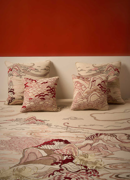 Four Viya Dreamscape Red Embroidered Cushion Covers (24"x24") featuring intricate wave and mountain motifs in beige, red, brown, and cream are arranged against a muted wall with a matching carpet and a bold burnt orange background.