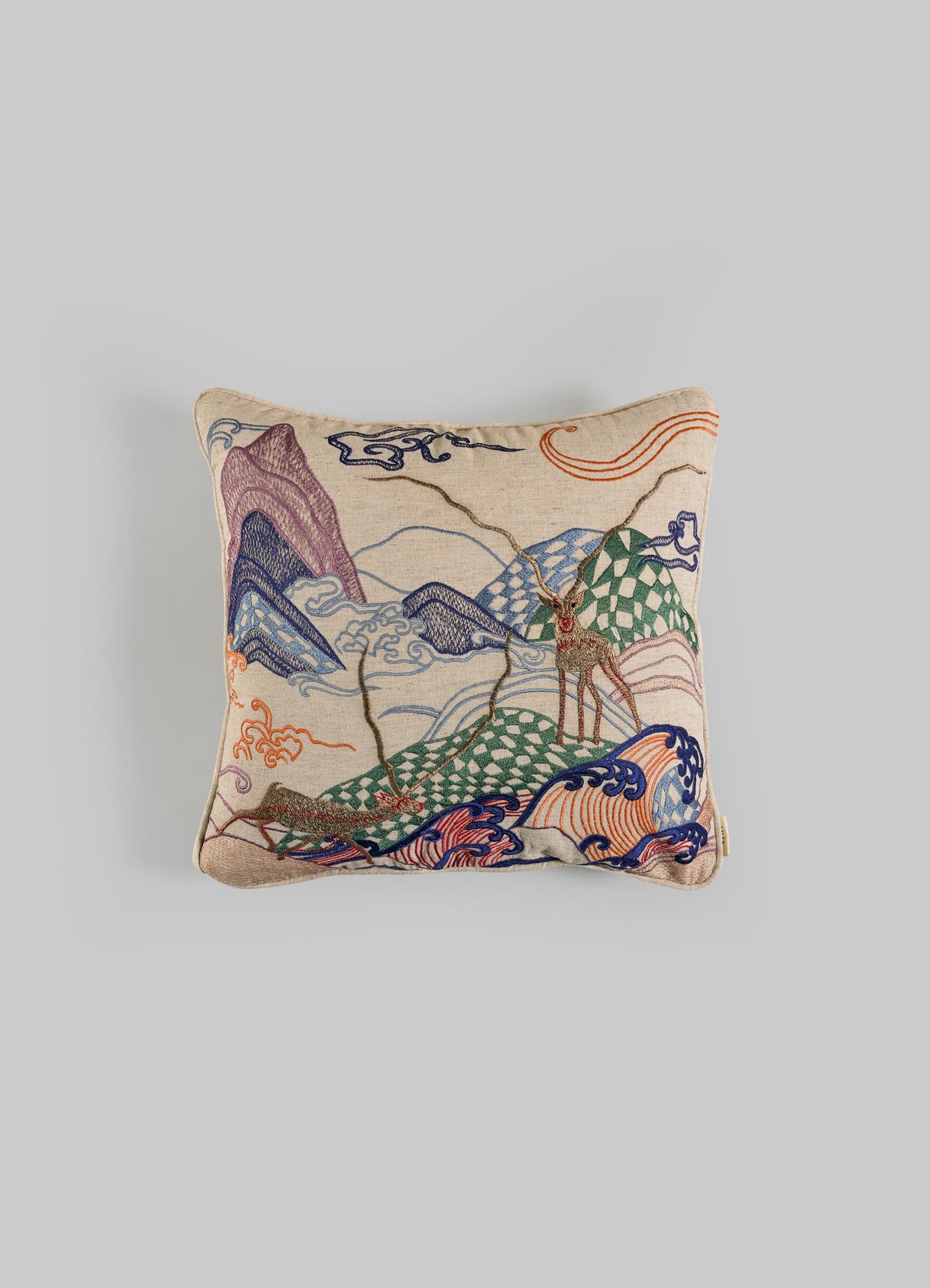 The Viya Dreamscape Blackbuck Multicolour Embroidered Cushion Cover 16"x16" features vibrant mountain, cloud, and deer motifs on beige fabric, inspired by symbolic designs and shown against a light gray background.