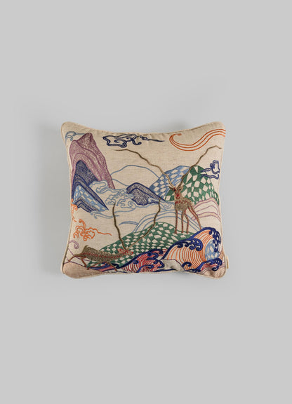 The Viya Dreamscape Blackbuck Multicolour Embroidered Cushion Cover 16"x16" features vibrant mountain, cloud, and deer motifs on beige fabric, inspired by symbolic designs and shown against a light gray background.