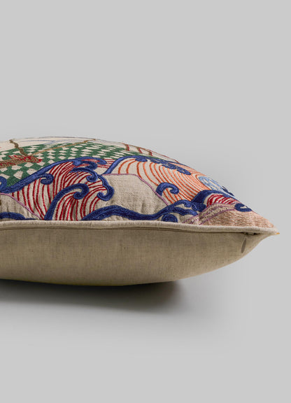 The Viya Dreamscape Blackbuck Multicolour Embroidered Cushion Cover (16"x16") has a beige base with green, red, blue, and orange motifs, shown from a side angle against a plain gray background.