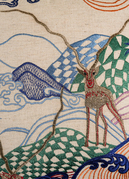 The Viya Dreamscape Blackbuck Multicolour Embroidered Cushion Cover (16"x16") features a deer with large antlers amid waves and geometric hills in blue, green, and red on cream fabric, inspired by symbolic textile motifs.