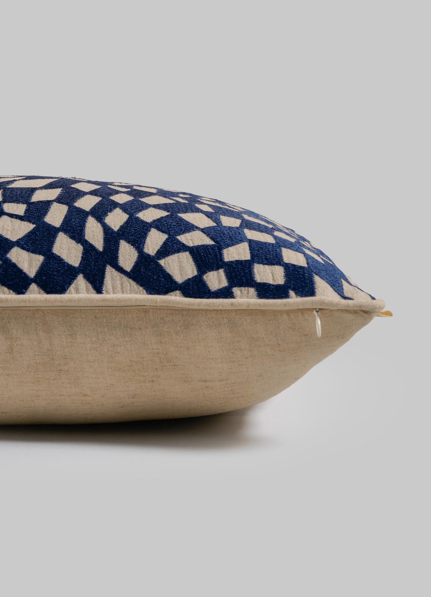 The Viya Dreamscape Blue Embroidered Checks Cushion Cover (12"x18") is seen from the side against a light gray background, showcasing its thickness, textured embroidery, and striking navy blue geometric pattern on beige fabric.