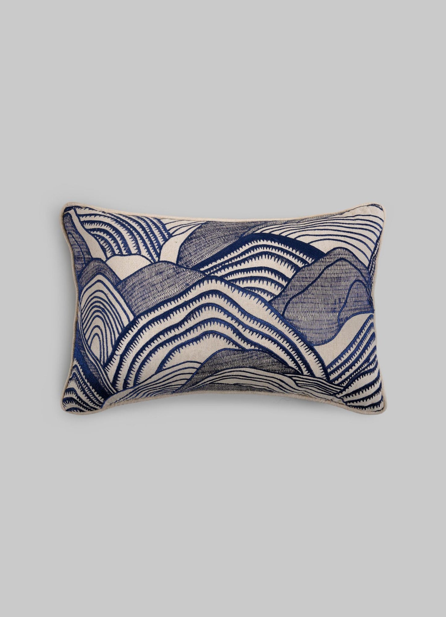The Viya Dreamscape Blue Embroidered Mounds Cushion Cover 12"x18" features symbolic blue and white wavy motifs, reminiscent of abstract mountains or waves, on a plain light gray background.