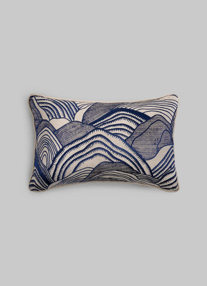 The Viya Dreamscape Blue Embroidered Mounds Cushion Cover 12"x18" features symbolic blue and white wavy motifs, reminiscent of abstract mountains or waves, on a plain light gray background.