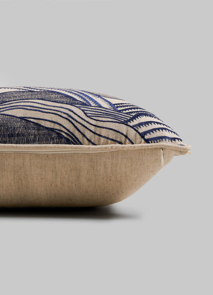 A close-up side view of the Viya Dreamscape Blue Embroidered Mounds Cushion Cover (12"x18") shows its beige fabric with blue geometric motifs and a visible zipper along the edge, set against a plain gray background.