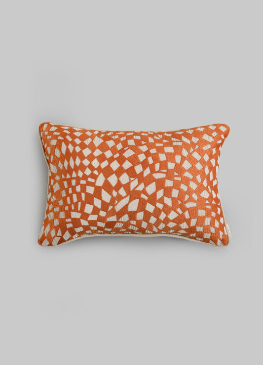 The Viya Dreamscape Orange Embroidered Checks Cushion Cover (12"x18") features an orange background with irregular cream geometric motifs inspired by embroidered textiles, creating a mosaic-like pattern, shown on a light gray surface.