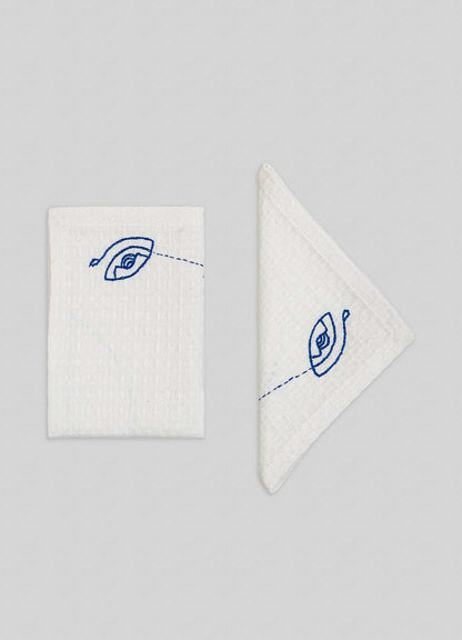 Viya’s Evil Eye Hand Embroidered Ecru Face Towels (set of 4) feature intricate blue Nazar motif designs on white fabric, with one towel folded to display the full eye and another showing part of this protective symbol on a light gray background.