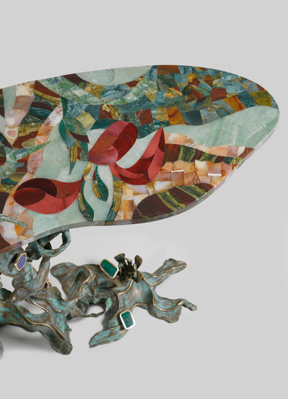 The VIYA Glory Lily Multicolour Console Table features a vibrant mosaic tabletop inspired by the Glory Lily flower and a sculpted cast brass base with green stones and an organic, flowing design.