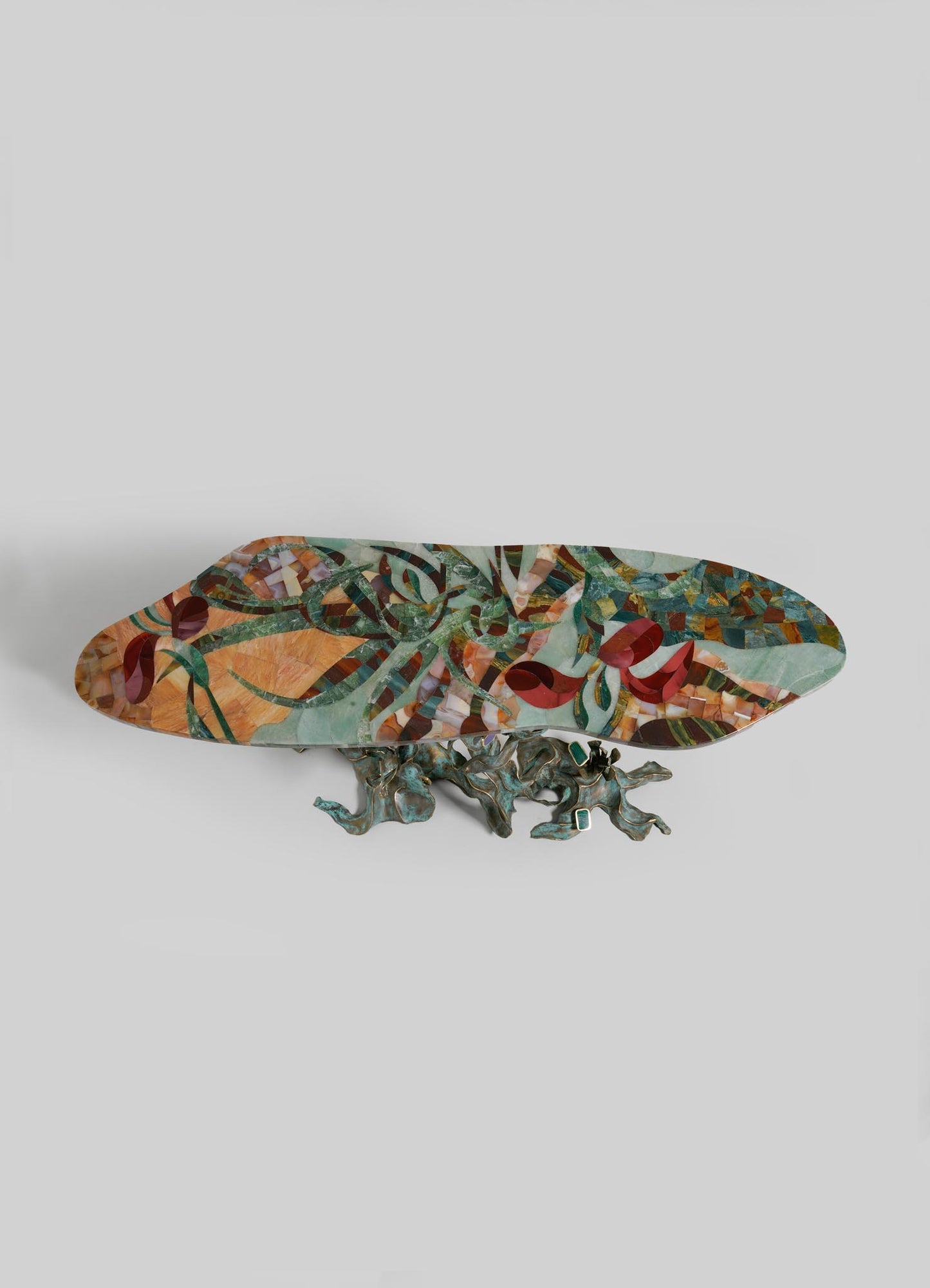 The VIYA Glory Lily Multicolour Console Table features a vibrant, abstract-patterned oval top set on an intricate sculptural cast brass base shaped like intertwined branches, inspired by the Glory Lily flower, shown against a light gray background.