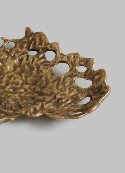 A close-up of VIYA's Golden Coral Bowl, featuring a textured, organic brass surface with irregular holes along the rim, displayed against a plain gray background.