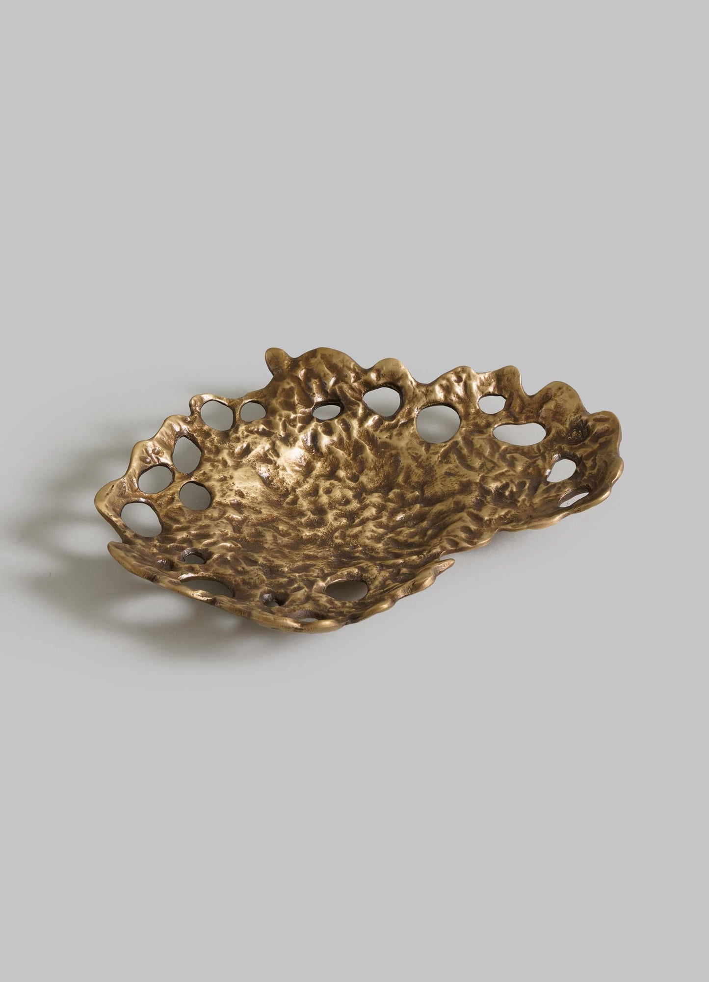 The VIYA Golden Coral Bowl features a decorative, irregular bronze design with a textured surface and various-sized holes around the rim, showcased against a light gray background.