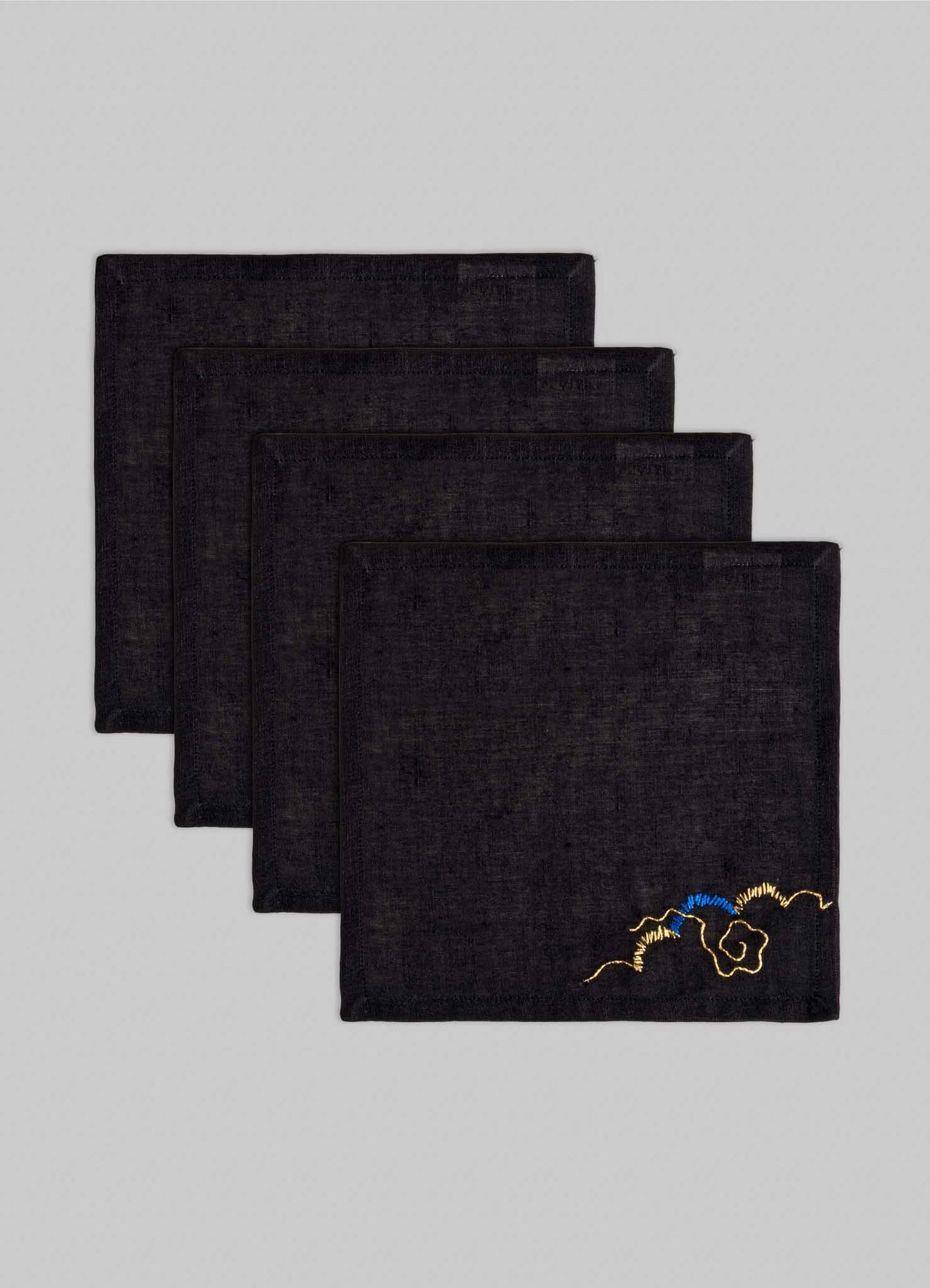 The Viya Gajasimha Hand Embroidered Black & Gold Cocktail Napkins (Set of 4) are neatly stacked, each featuring a gold embroidery inspired by ancient Indian art, set against a light gray background.