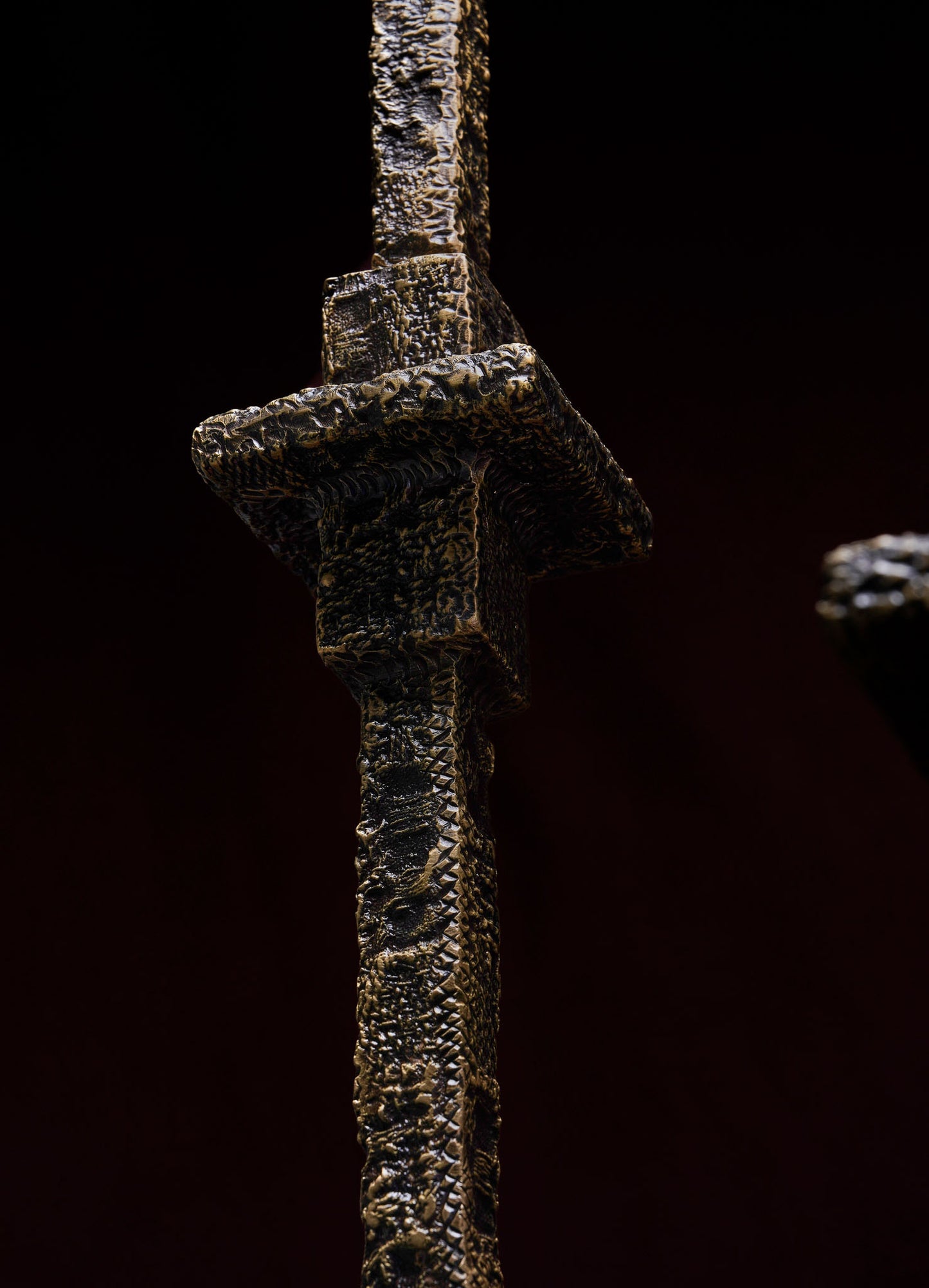 Close-up of the VIYA Tiruppur Totem Candle Holder Large, showcasing its textured, metallic dark finish and geometric design with rough, brocade-like surfaces and angular forms set against a dark background.