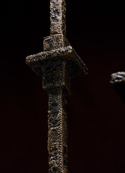 Close-up of the Tiruppur Totem Candle Holder Small by VIYA, showcasing its textured metallic cross-shaped form and dark finish. The design evokes industrial style with subtle nods to Indian brocade and handwoven fabric patterns.