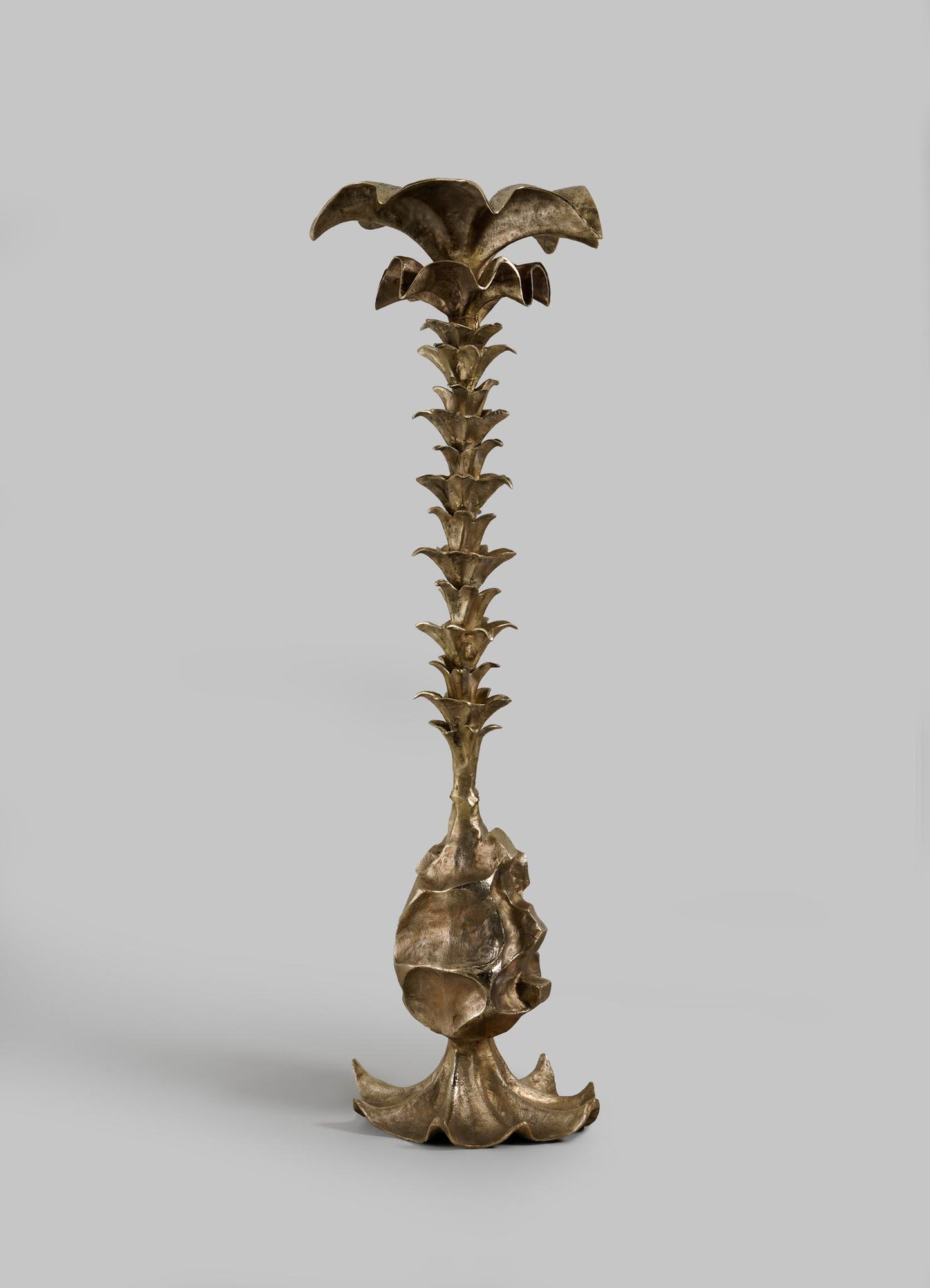 The VIYA Indian Vessel Finial is a bronze sculpture featuring a broad, petal-like base, leaf-like accents, and a flower-shaped top—evoking the elegance of traditional brass Indian decor—displayed against a plain gray background.