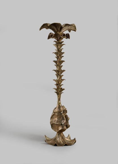 The VIYA Indian Vessel Finial is a bronze sculpture featuring a broad, petal-like base, leaf-like accents, and a flower-shaped top—evoking the elegance of traditional brass Indian decor—displayed against a plain gray background.
