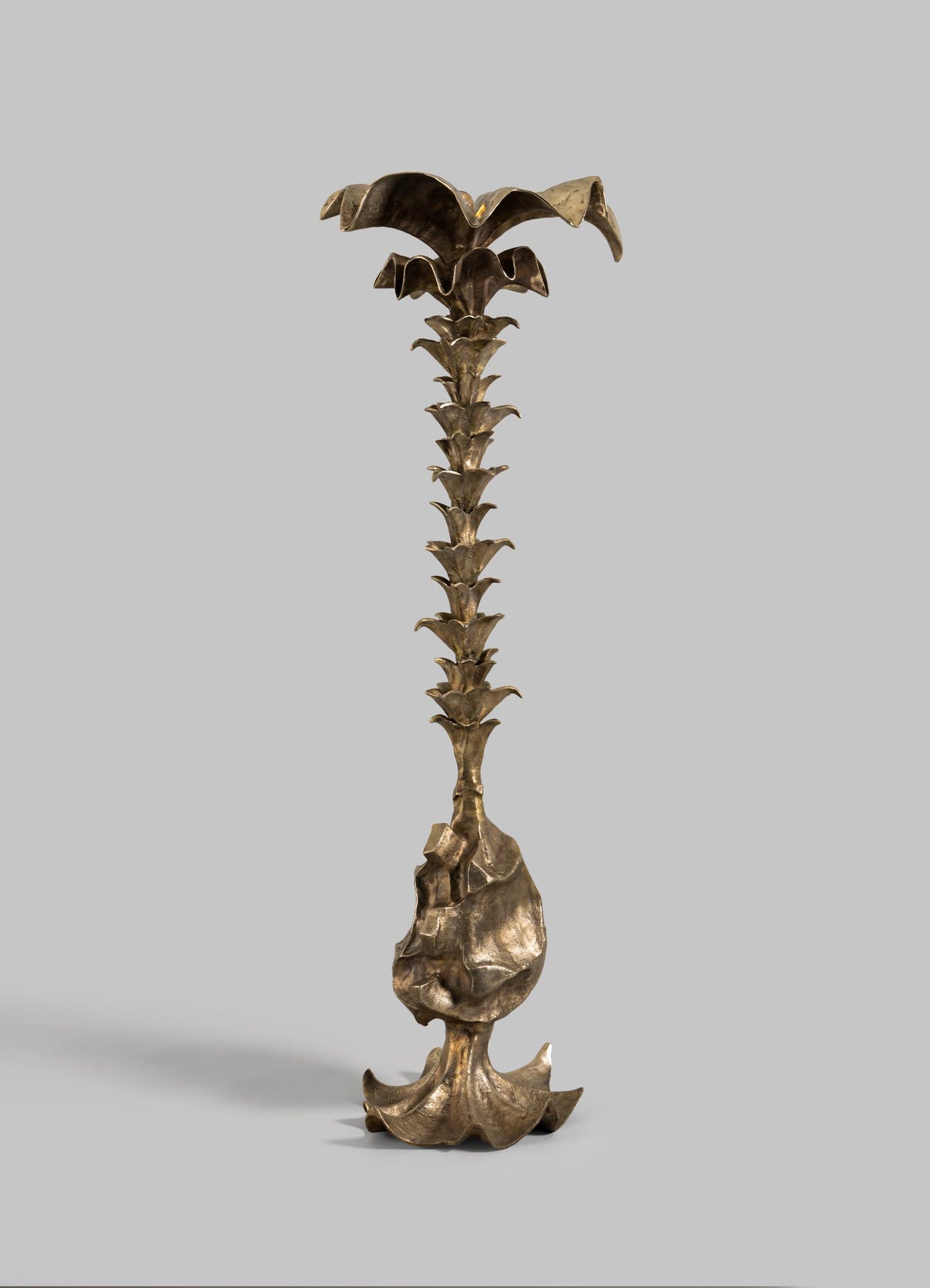 The VIYA Indian Vessel Finial is a tall, bronze sculpture inspired by Indian decor, featuring a stylized palm tree with broad leaves and a textured base, shown against a plain gray background.