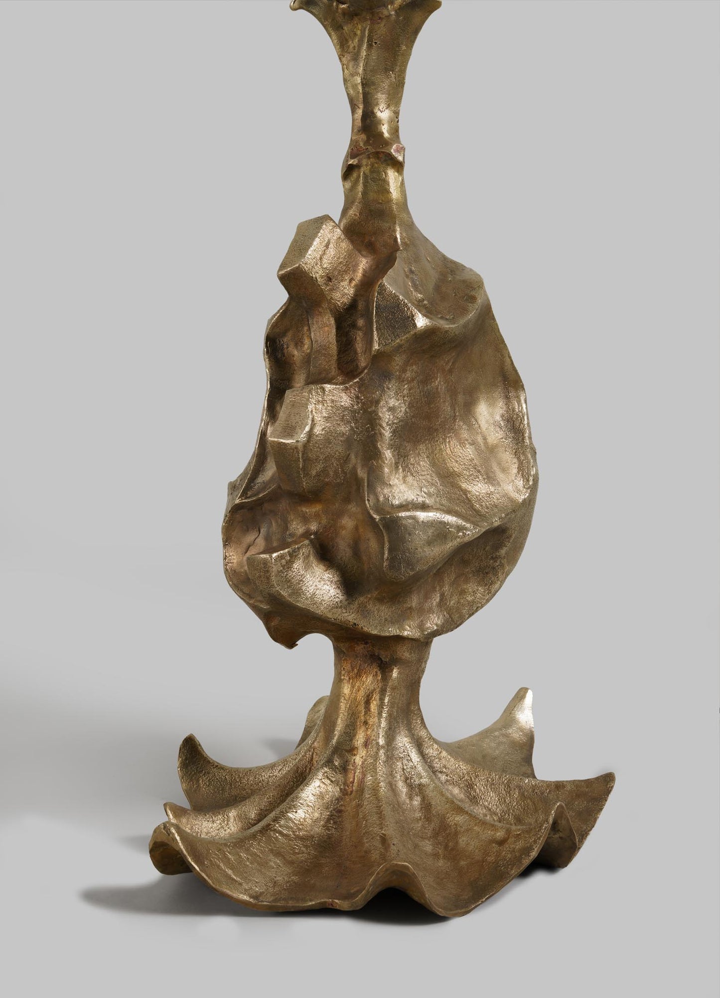 The VIYA Indian Vessel Finial is a bronze abstract sculpture with an organic, textured surface and irregular shapes, featuring a curving base that widens and flattens at the bottom, set against a plain gray background.