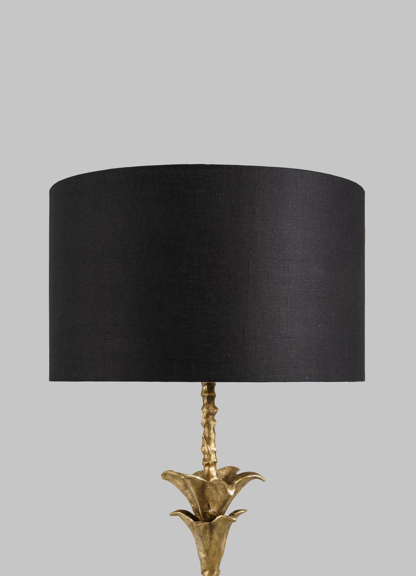 The VIYA Indian Vessel Floor Lamp features a black cylindrical lampshade and a gold flower-shaped base inspired by traditional brass vessels, displayed against a plain light gray background.