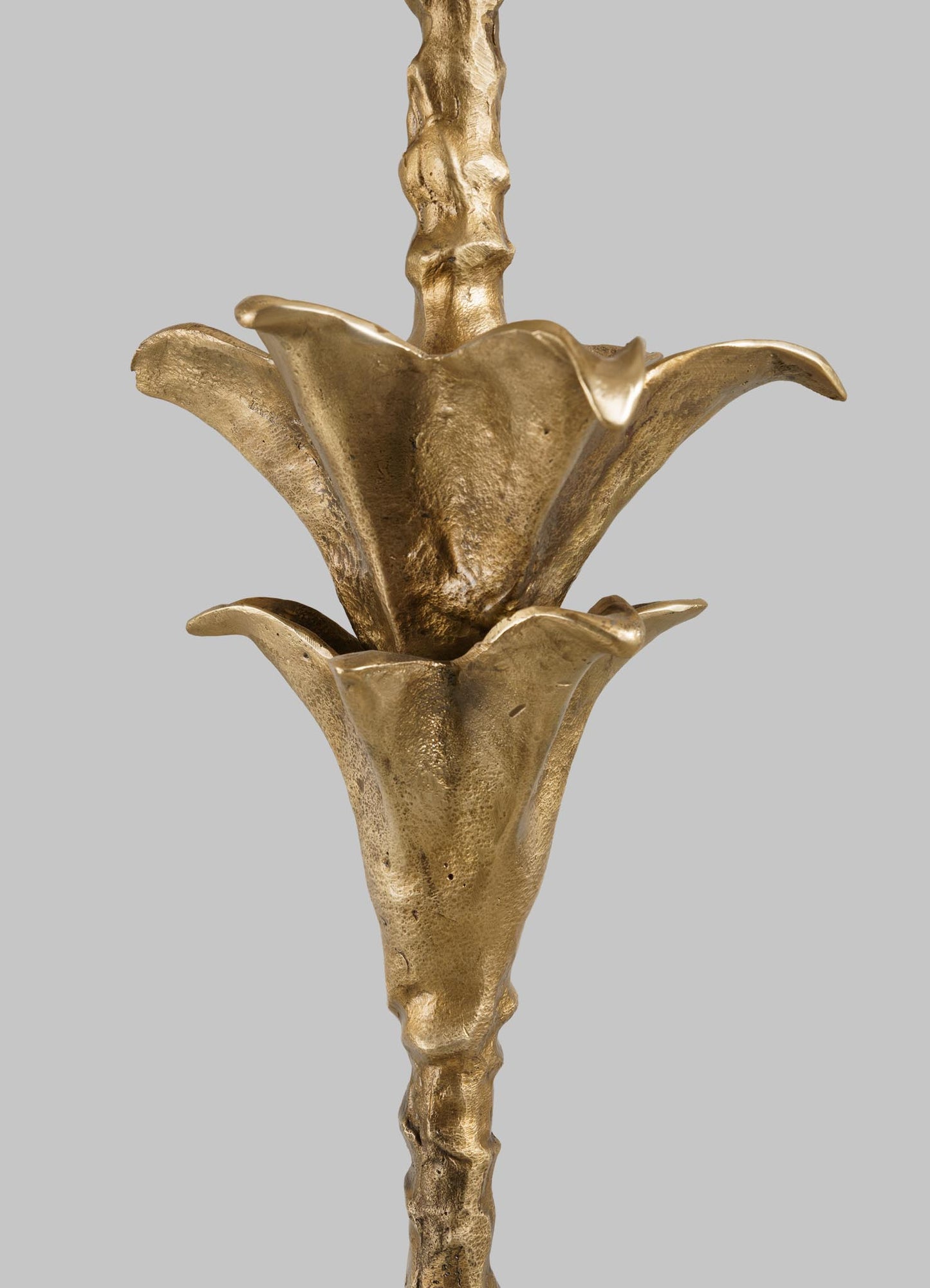 Close-up of the VIYA Indian Vessel Floor Lamp, a metallic gold sculpture with two trumpet-shaped flowers and textured stems, inspired by traditional Indian brass vessels like the lota and surahi, set against a light gray background.