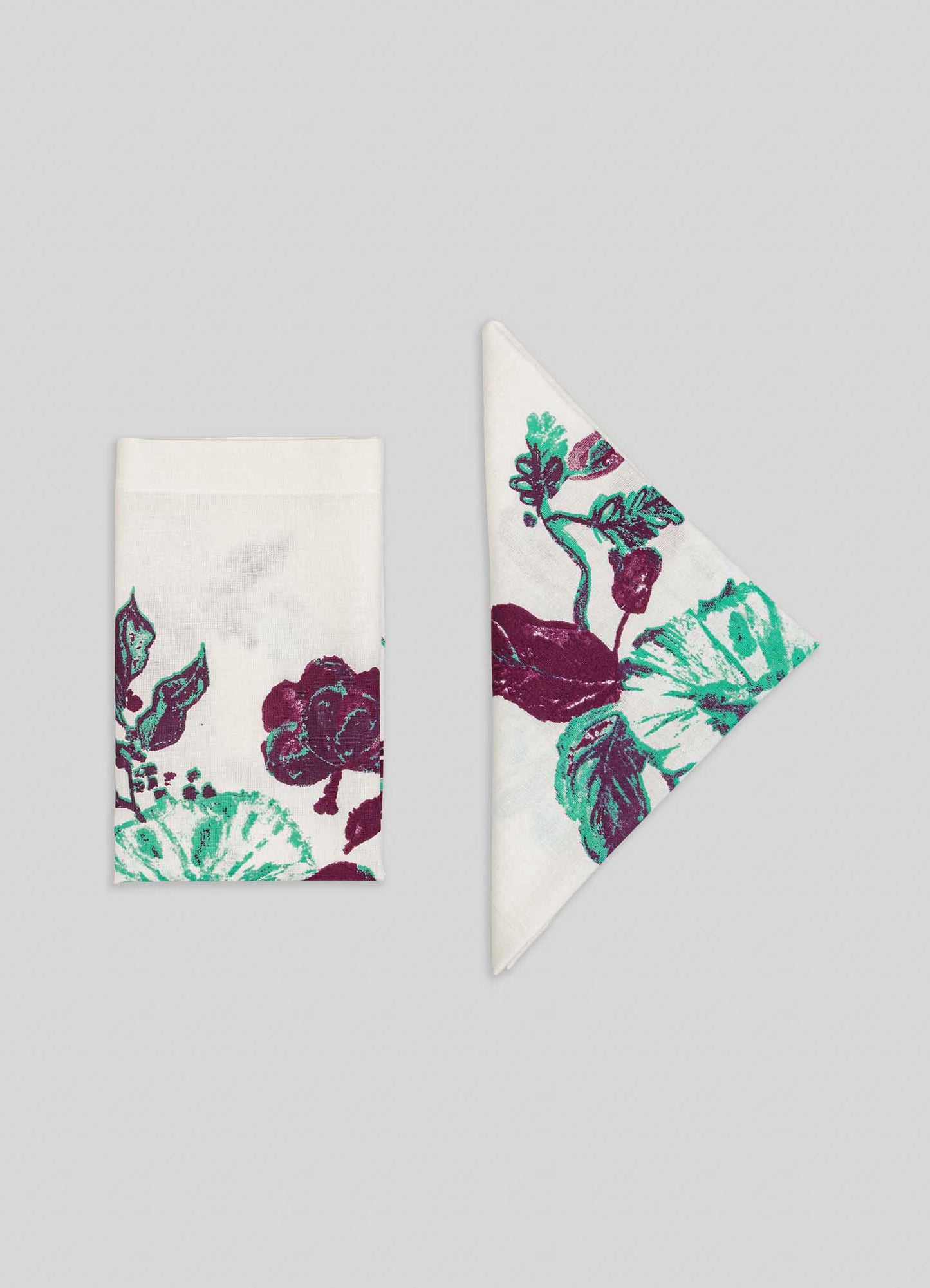 Two Jackfruit Green Napkins from Viya, inspired by Indian fruit orchards, feature green and burgundy florals; one is folded into a rectangle, the other into a triangle, both displayed on a light gray background.