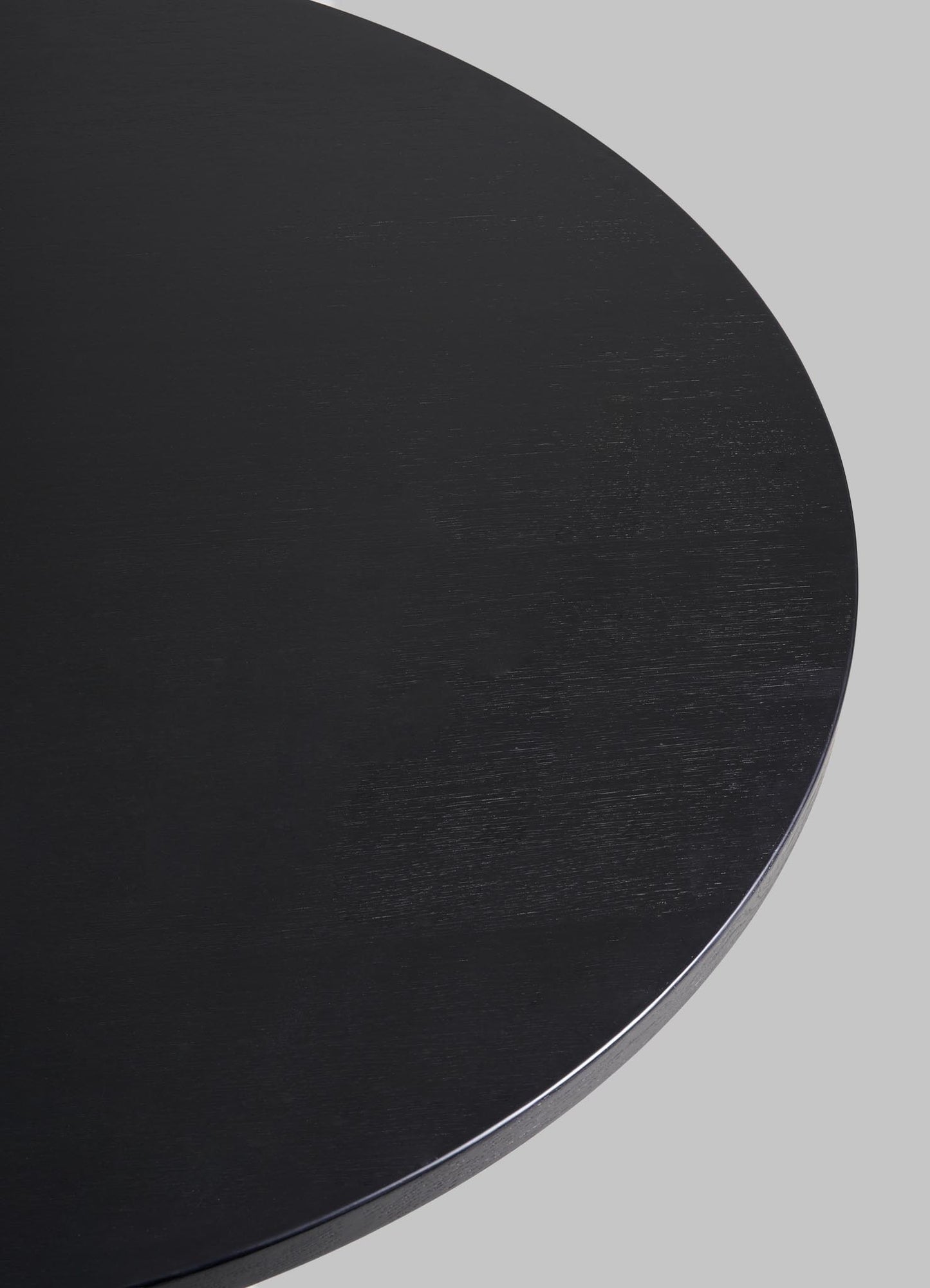 A close-up of the edge of the round, black Kikar Dining Table by VIYA, part of our desert collection, set against a plain gray background.