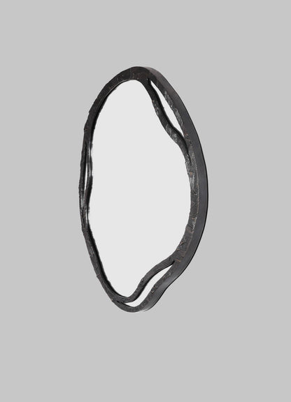 The VIYA Kolam Bronze Mirror Round Large features an artistic, irregular sculpted metal frame with wavy edges, inspired by Indian Kolam patterns. Shown against a plain gray background.