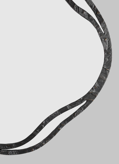 The VIYA Kolam Bronze Mirror Round Large features a curved, black textured metal frame with organic lines inspired by Indian Kolam patterns, partially surrounding a clear round mirror against a plain gray background.