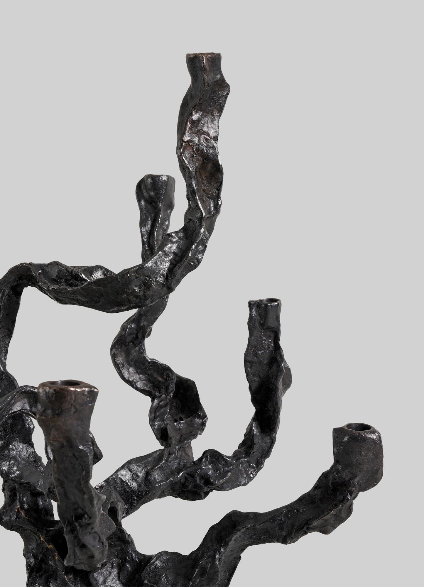 A close-up of the VIYA Meghalaya Candelabra Large, a dark and textured metal sculpture inspired by abstract tree branches and living root bridges, showcased against a plain light gray background.