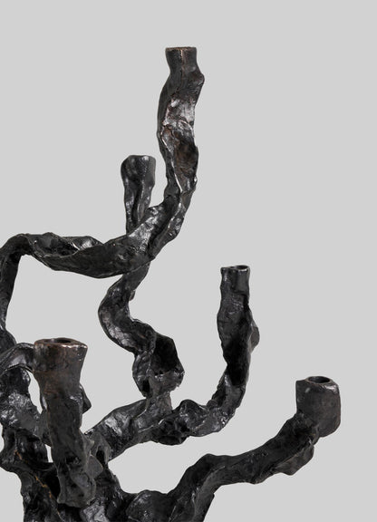 A close-up of the VIYA Meghalaya Candelabra Large, a dark and textured metal sculpture inspired by abstract tree branches and living root bridges, showcased against a plain light gray background.