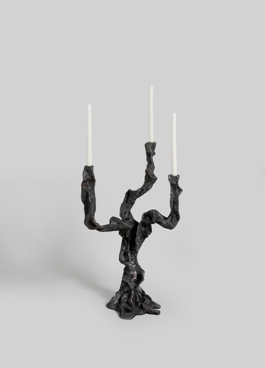 The VIYA Living Roots Candelabra Small features three twisted, branch-like black arms holding white taper candles, set against a simple light gray background.