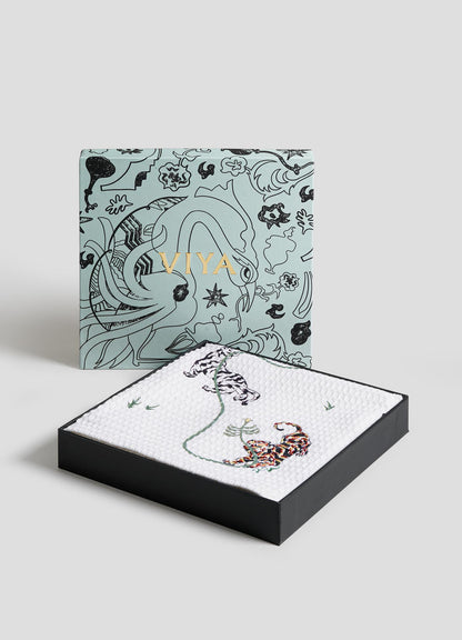 The Lounging Tiger Hand Towels - Set of 2 by Viya are displayed in a decorative box with floral and tiger designs, alongside a matching tray featuring two tigers and a flower, set on a white textured surface against a light background.