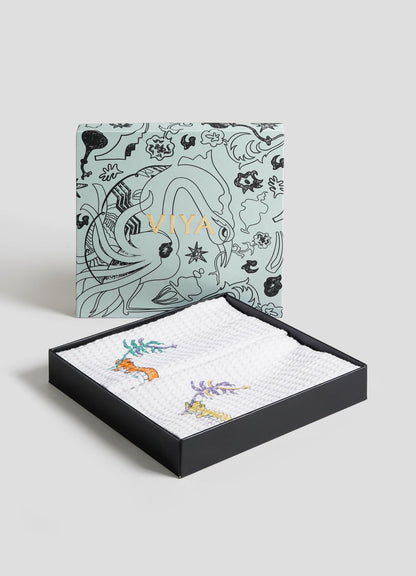 The Lurking Crocodile Hand Towels by Viya come as a set of 2, packaged in a decorative black box with "Viya" in gold, featuring folded white towels embroidered with vibrant aquatic animals and plants.