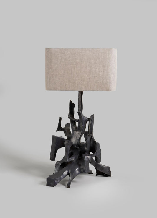 The VIYA Maski Table Lamp features a sculptural black base resembling abstract tree roots and a rectangular beige fabric shade, shown against a plain light gray background.