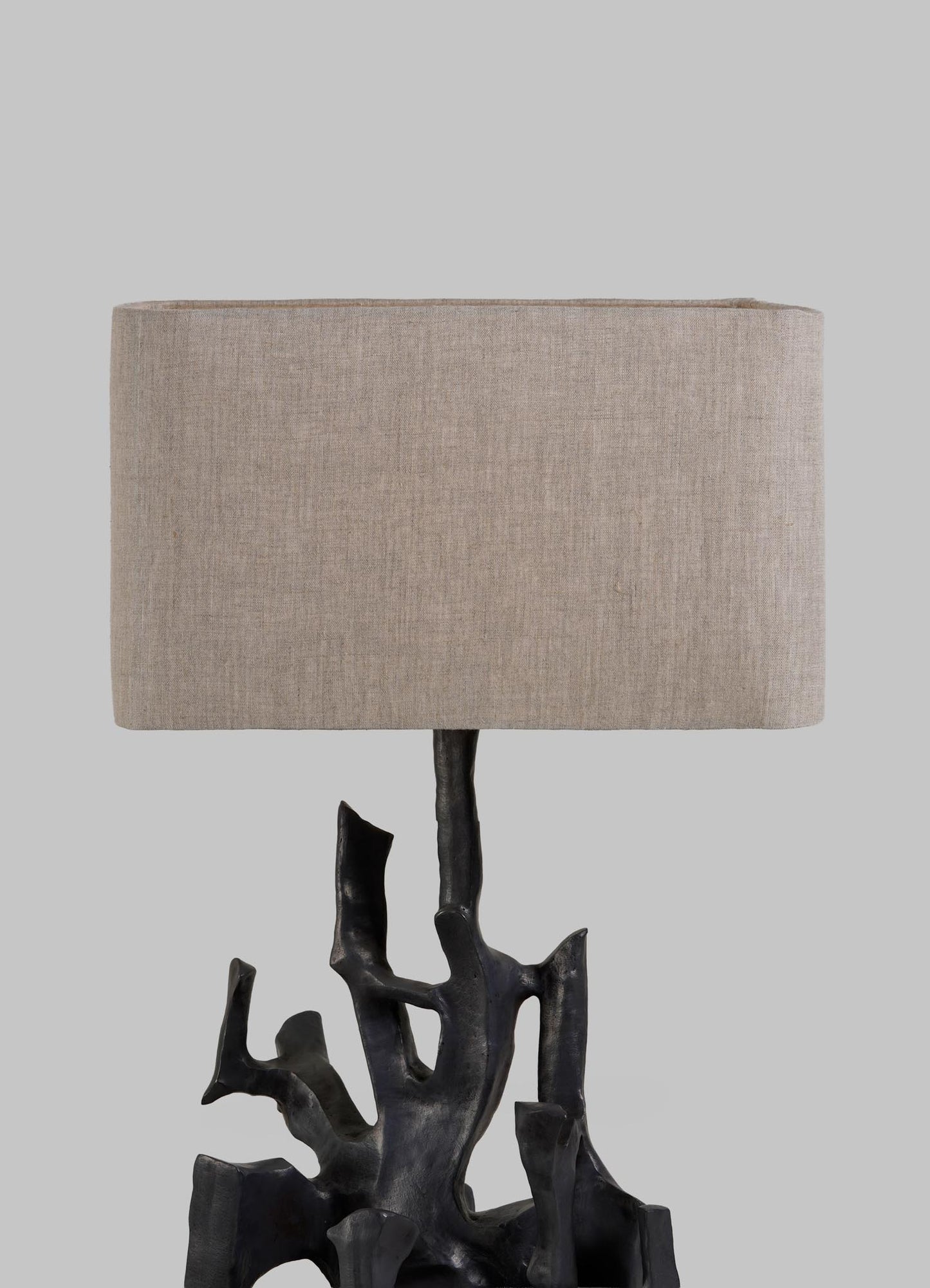 The Maski Table Lamp by VIYA features a sculptural black base resembling intertwined branches and a rectangular beige fabric shade, set against a plain gray background.