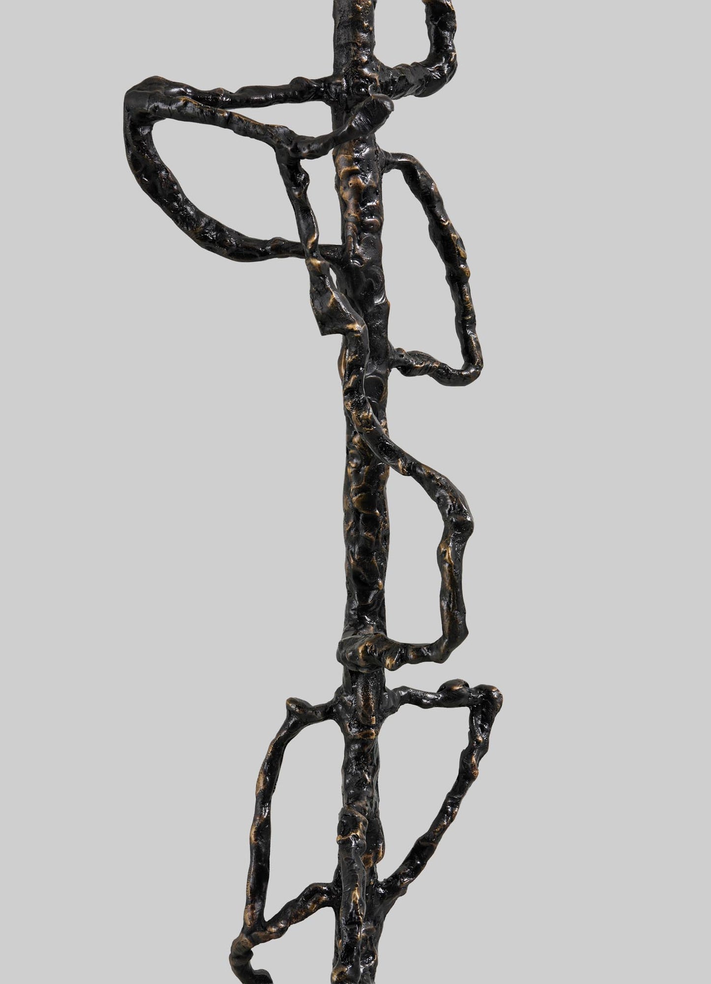 A close-up of the Mohenjo Daro Floor Lamp by VIYA, an abstract black metal design with irregular, interconnected loops and vertical segments, reminiscent of ancient relics, displayed against a plain light gray background.