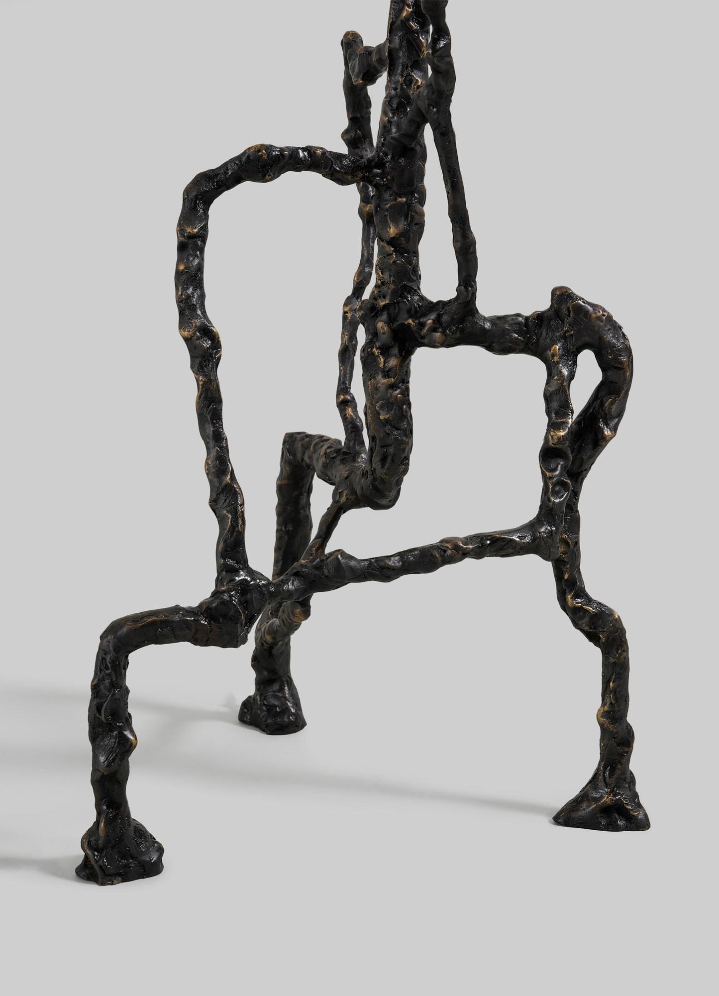 The VIYA Mohenjo Daro Floor Lamp is a black metal sculpture with irregular, textured rods forming a seated figure with elongated limbs, evoking ancient artistry. It stands out against a plain light gray background.