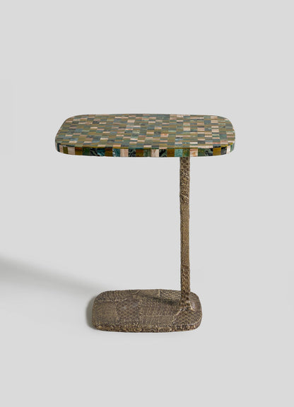 The VIYA Mosaic Side Table A is a small modern table with a rectangular checkered green, black, and tan top, supported by a single textured brown leg and matching cast brass base, set against a plain light background.