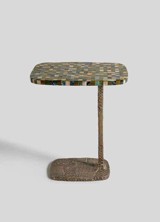 The VIYA Mosaic Side Table A is a small modern table with a rectangular checkered green, black, and tan top, supported by a single textured brown leg and matching cast brass base, set against a plain light background.