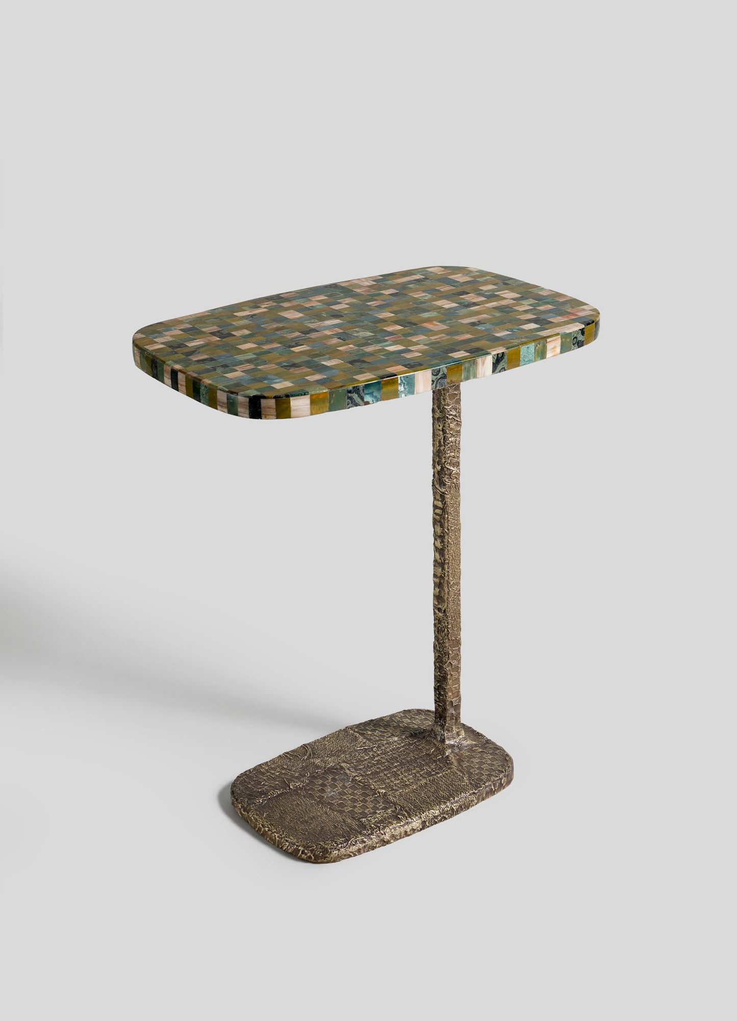 The VIYA Mosaic Side Table A features a rectangular, colorful mosaic top, supported by a single textured metal leg and a matching cast brass base, displayed against a plain white background.