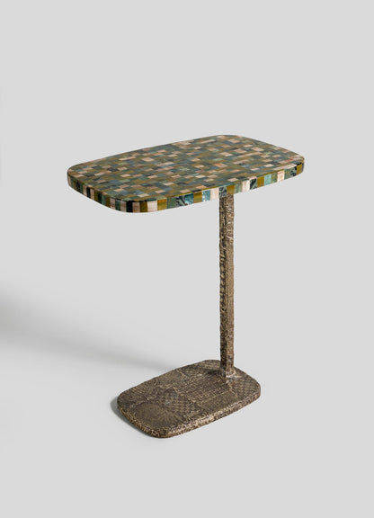 The VIYA Mosaic Side Table A features a rectangular, colorful mosaic top, supported by a single textured metal leg and a matching cast brass base, displayed against a plain white background.