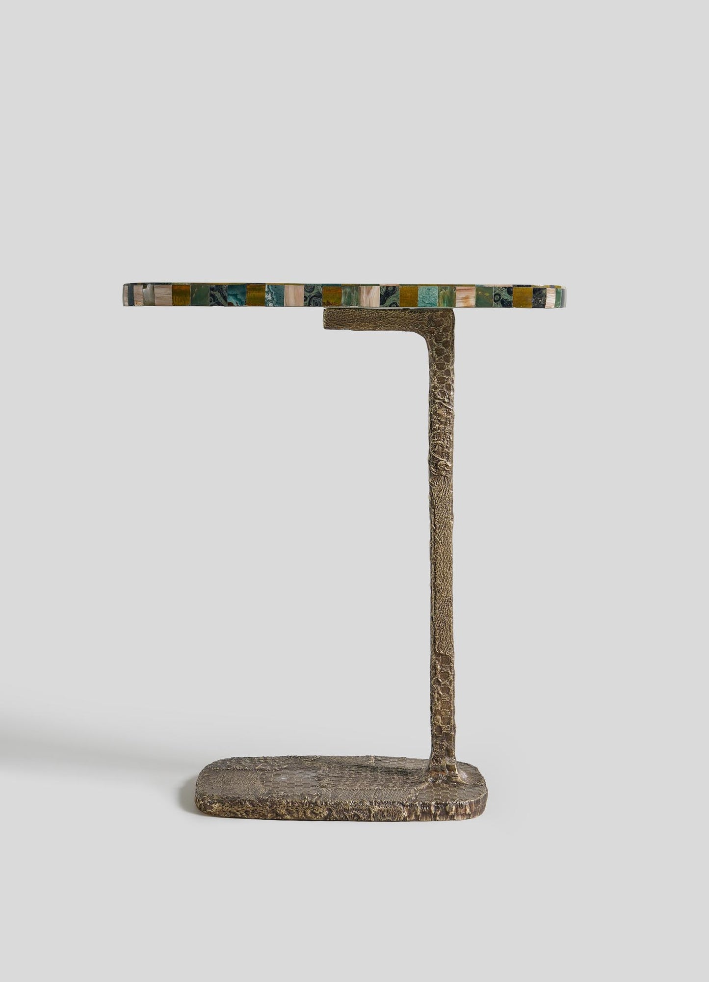 The VIYA Mosaic Side Table A is a small table with a textured cast brass base and a round, multicolored semi-precious stone top, shown against a plain light gray background.