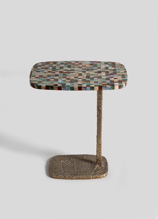 The VIYA Mosaic Side Table B features a small rectangular top with multicolored square tiles, set on a single textured metal leg and an irregular cast brass base, displayed against a plain light background.