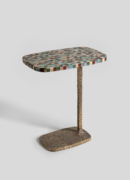 The VIYA Mosaic Side Table B features a colorful mosaic-patterned rectangular top made of semi-precious stones, with a single textured gold support and matching oval cast brass base, shown against a plain light gray background.