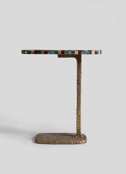 The VIYA Mosaic Side Table B features a round top with a multicolored mosaic tile edge, set on a slim, rectangular cast brass base with textured gold-tone vertical support. The background is plain light gray.
